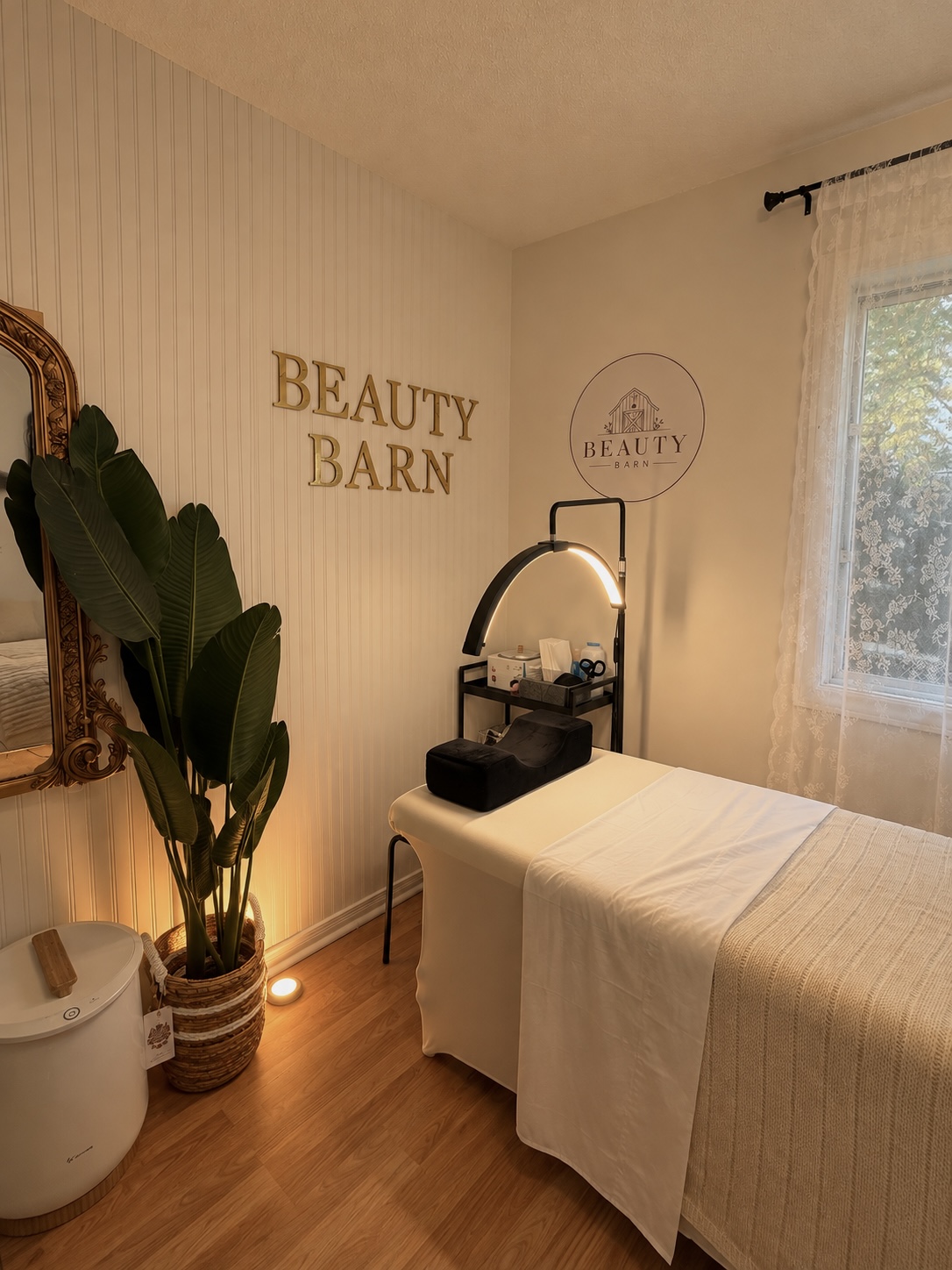 Beauty Barn’s treatment room with a soft-lit lash bed, an arched LED lamp and gold Beauty Barn lettering on the wall